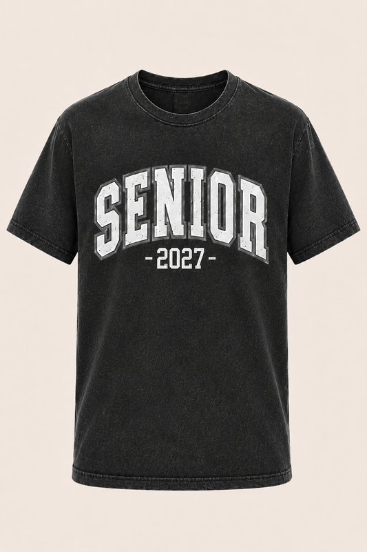 A black acid-wash short-sleeve t-shirt with 'SENIOR -2027-' printed in white varsity block letters on the front, displayed against a solid light beige background.